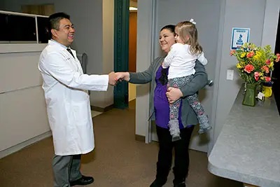 Dr. Tony Lu shaking hands with a woman carrying her child