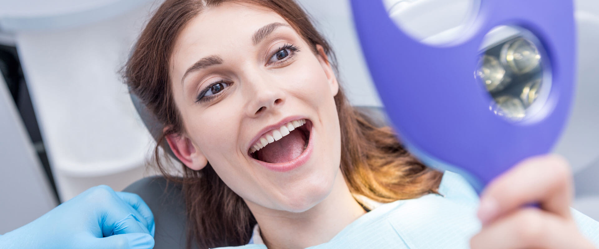 Excited female patient looking at her teeth in a hand mirror after teledentistry